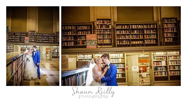 Couple in wedding attire embracing in a library aisle with bookshelves behind them