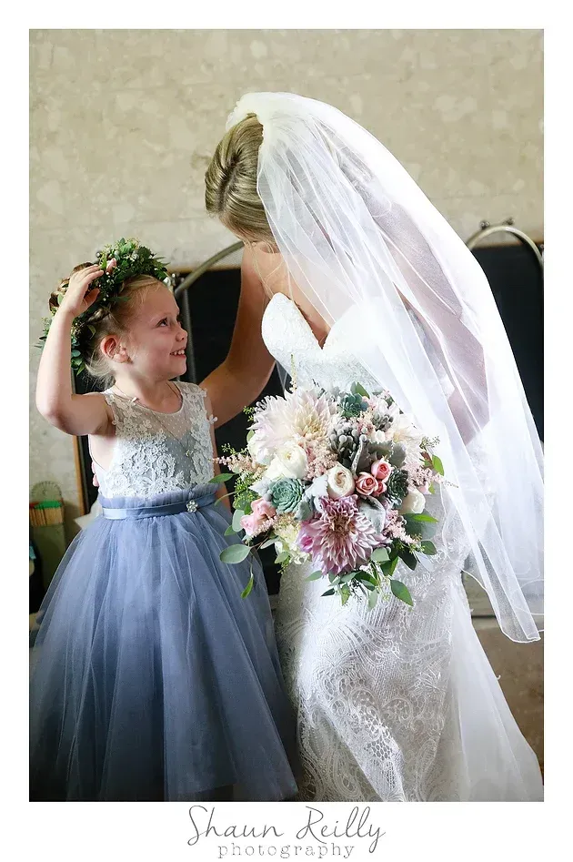 Bride holding bouquet while a young girl in a gray dress raises her arms beside her under a veil