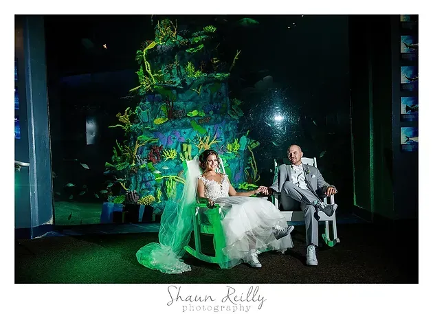 Bride and groom seated in glowing green chairs before a colorful projection backdrop
