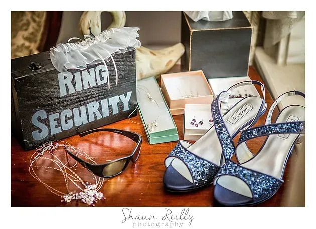 Wedding accessories on a table, including a “Ring Security” sign, blue shoes, glasses, and a ring box