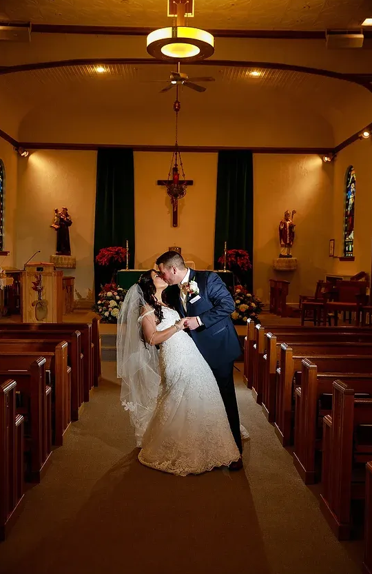 Bride and groom kissing in a church aisle under warm lighting