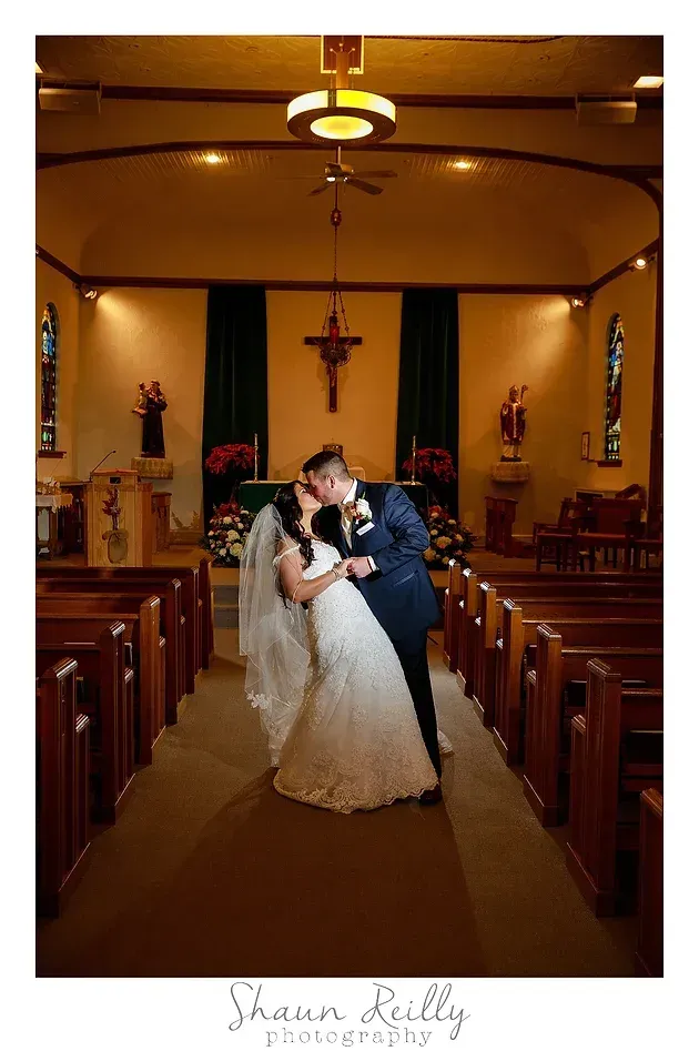 Bride and groom kissing in a church aisle, with pews and warm altar lighting