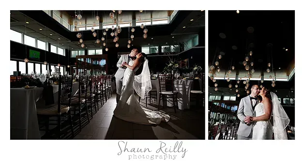 Bride and groom kissing in a dark, elegant ballroom with tall windows and chandeliers