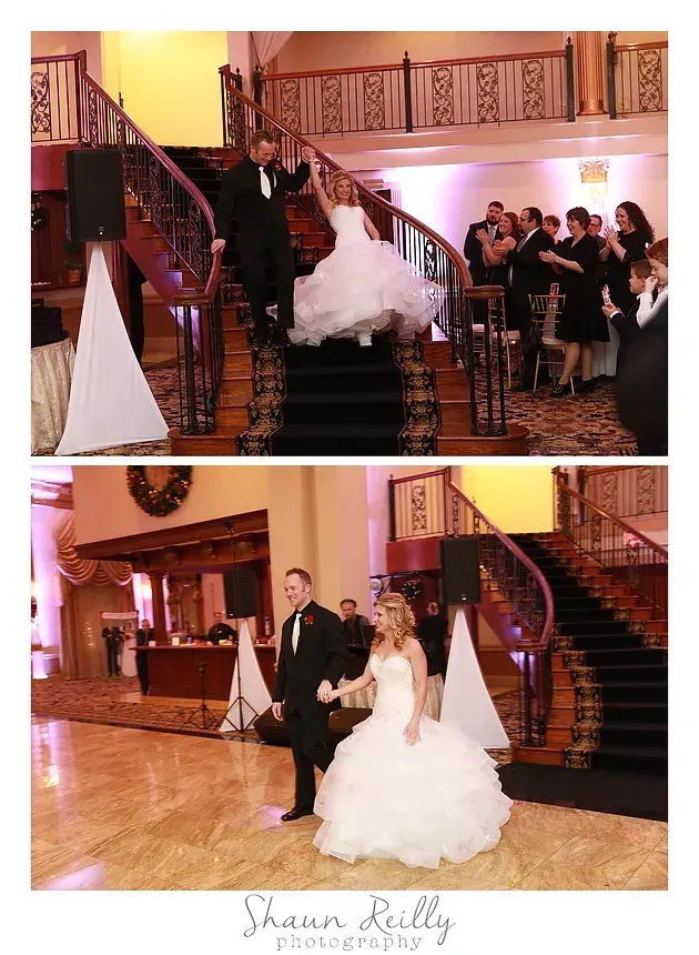 Wedding couple on staircase in formal indoor venue, with guests applauding nearby