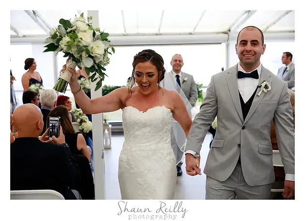 Bride and groom walking down the aisle, bride raising bouquet and smiling