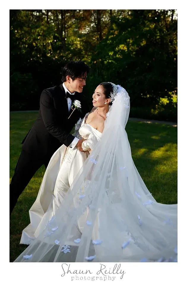 Bride and groom in black tuxedo and white gown smiling in a garden