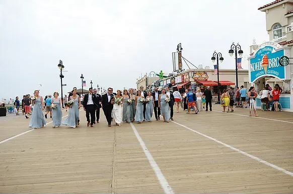 Group of people walking on a seaside boardwalk with amusement rides in the background