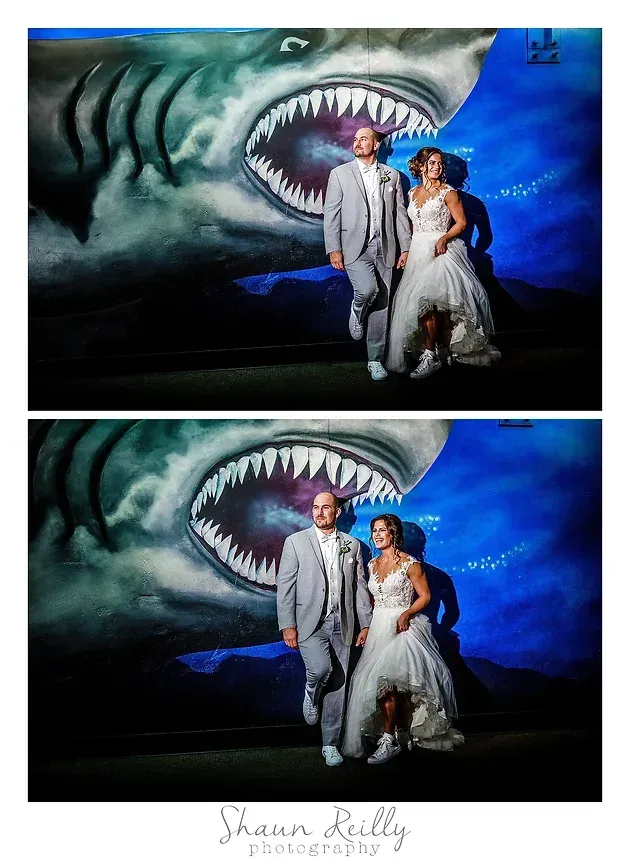 Couple posing in front of a giant shark mural at a wedding venue, in white wedding attire