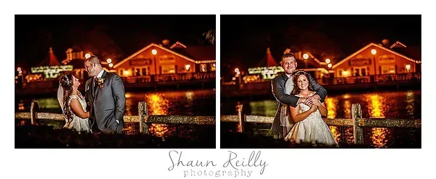 Couple in wedding attire posing at night by a lit waterfront building