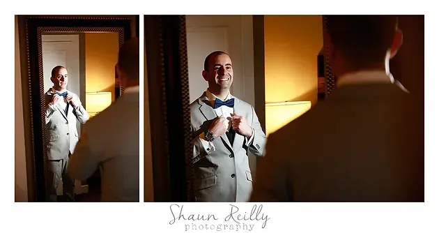 Bride admiring her reflection in a mirror, wearing a white dress in warm indoor light.