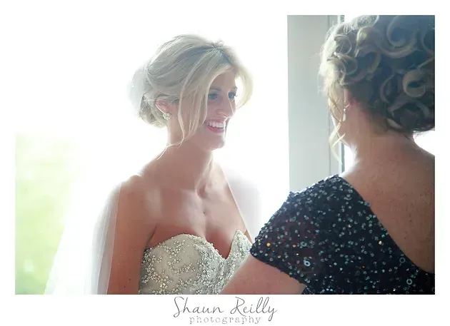 Bride smiling at herself in a mirror, wearing a strapless beaded wedding dress with an elegant updo.