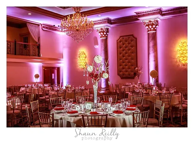 Elegant banquet hall with pink lighting, chandeliers, and round tables set for an event