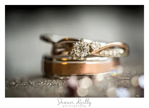 Wedding rings with a diamond engagement ring on a reflective surface, softly blurred background