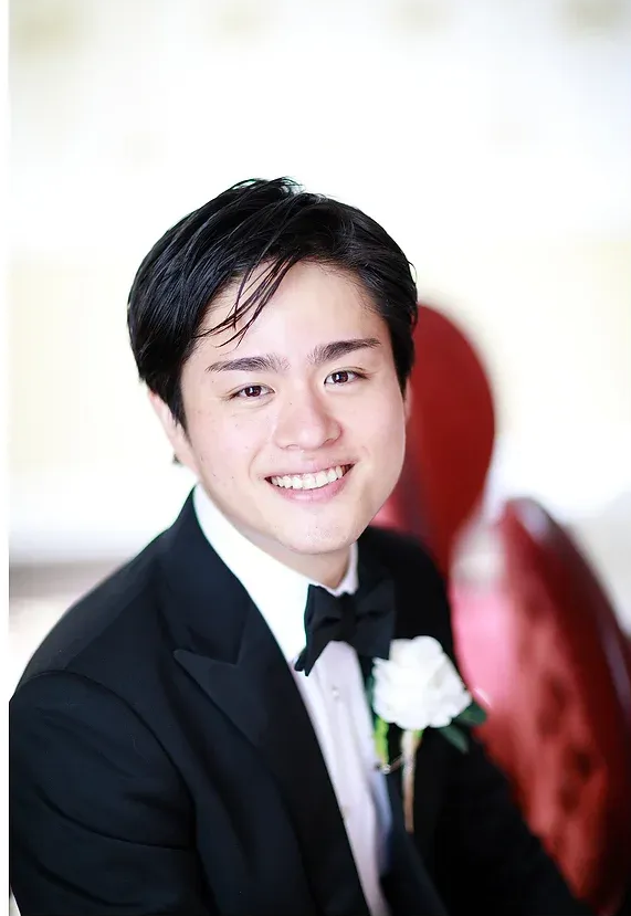 Smiling person in a black tuxedo with a white boutonniere at a formal event