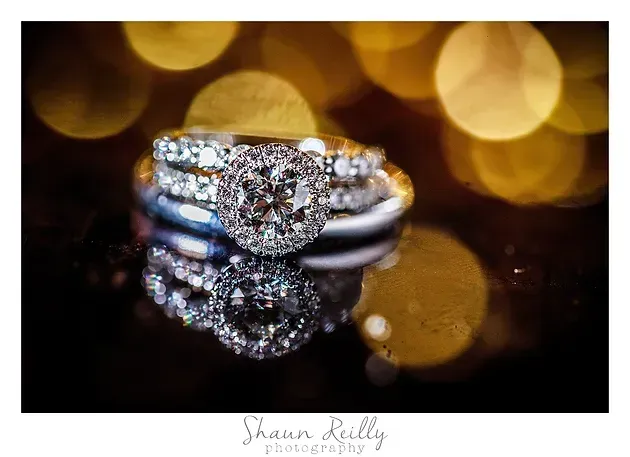 Diamond engagement ring on a reflective surface with warm gold bokeh lights in the background