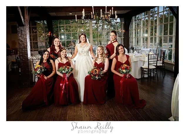 Bride with six bridesmaids in red dresses, posing indoors in a restaurant with floral bouquets