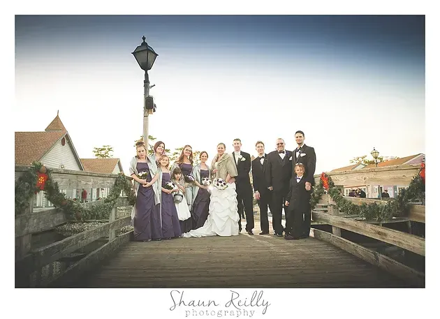 Wedding party posing on a bridge at sunset, with a bride in white and attendants in purple and black