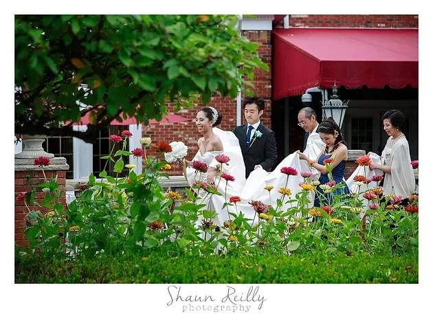 People walking with white and red decorations in front of a red awning and greenery