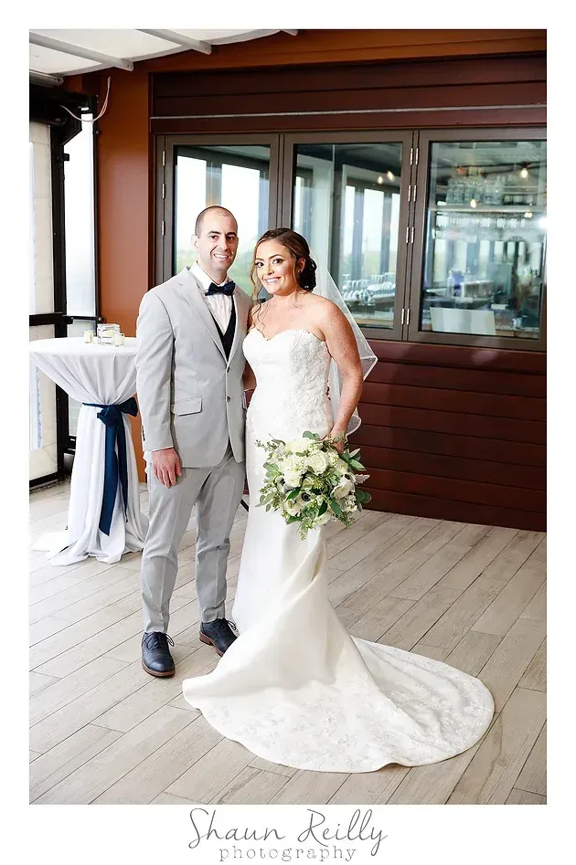 Bride and groom standing together indoors, bride holding a bouquet in a white gown