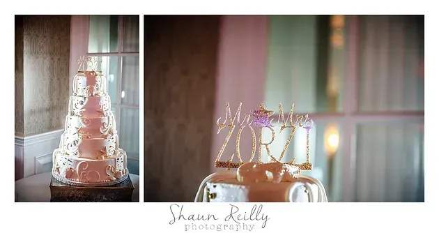 Pink wedding cake with tiered frosting, gold topper, and decorative candles on a table