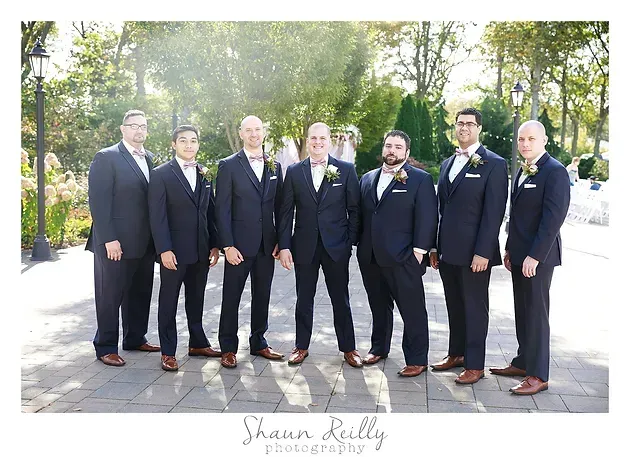 Seven people in dark suits standing outdoors on a sunlit path, posing for a formal group portrait.