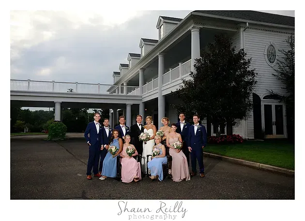 Group of people in formal attire posing outside a large white building with a covered walkway
