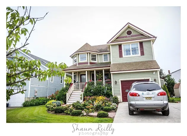 Two-story house with a red garage door, landscaped front yard, and a silver SUV in the driveway.