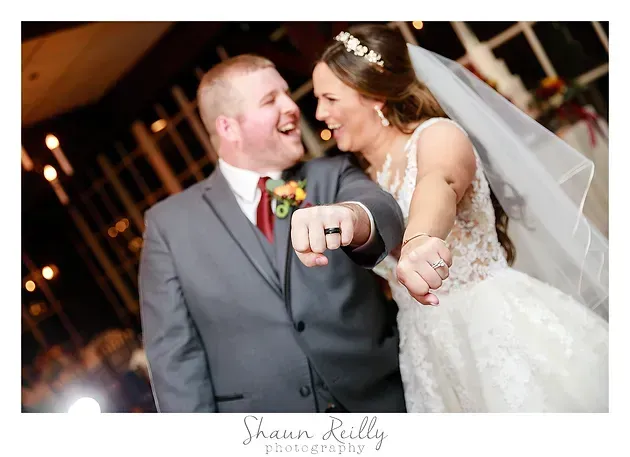 Bride and groom laughing, showing wedding rings at their reception