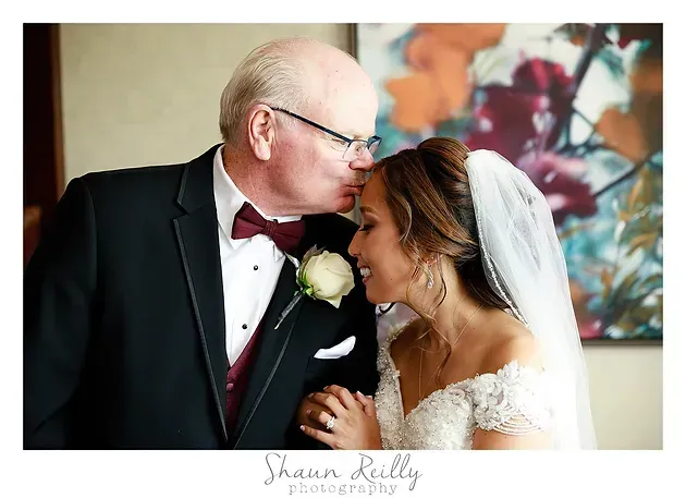 Man in tuxedo kissing bride in white veil at wedding, with floral background