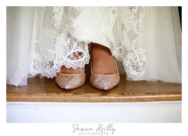 White lace wedding dress hem with glittery pink shoes on a wooden floor