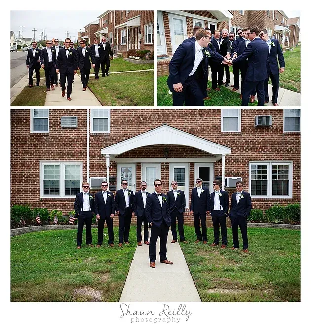 Men in dark suits posing outside a brick building, with one walking forward in front of the group