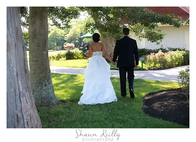 Bride in a white gown and groom in a black suit walking hand in hand in a garden