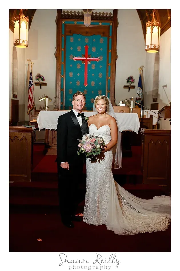 Bride and groom posing in a church before a turquoise altar, holding a bouquet and smiling