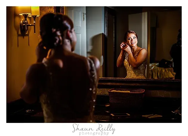 Woman adjusting her earring in a mirror, warmly lit bathroom with a vanity and reflection.
