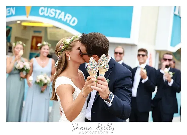 Newlyweds kissing and sharing ice cream cones outside a custard shop during their wedding celebration