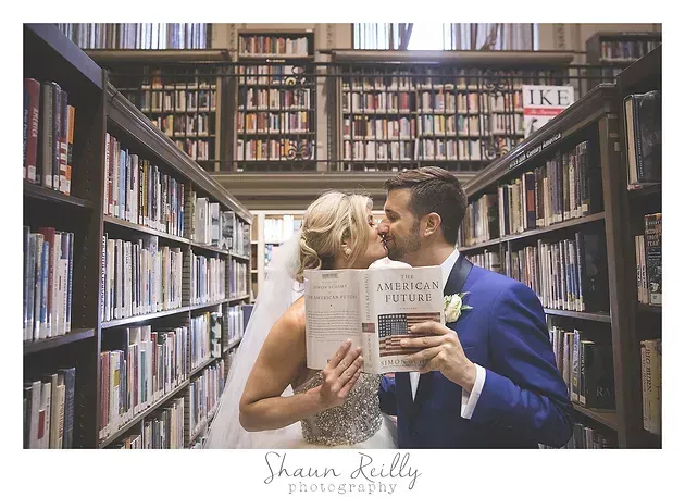 Couple kissing in a library aisle while holding a book