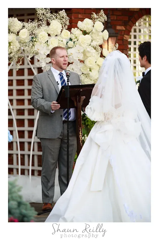 Wedding ceremony with officiant and bride under white floral arch