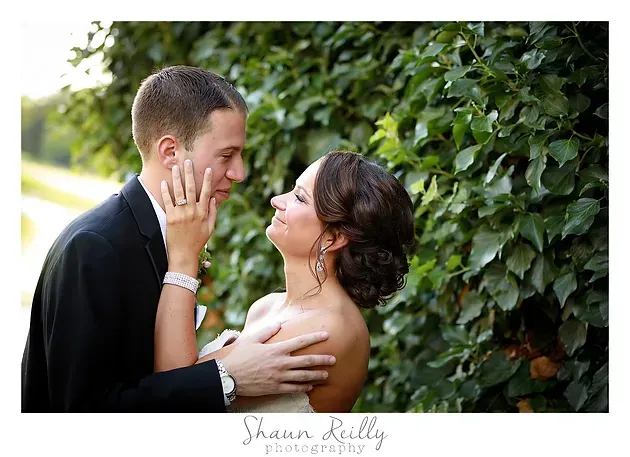 Couple embracing and gazing at each other beside a leafy green hedge