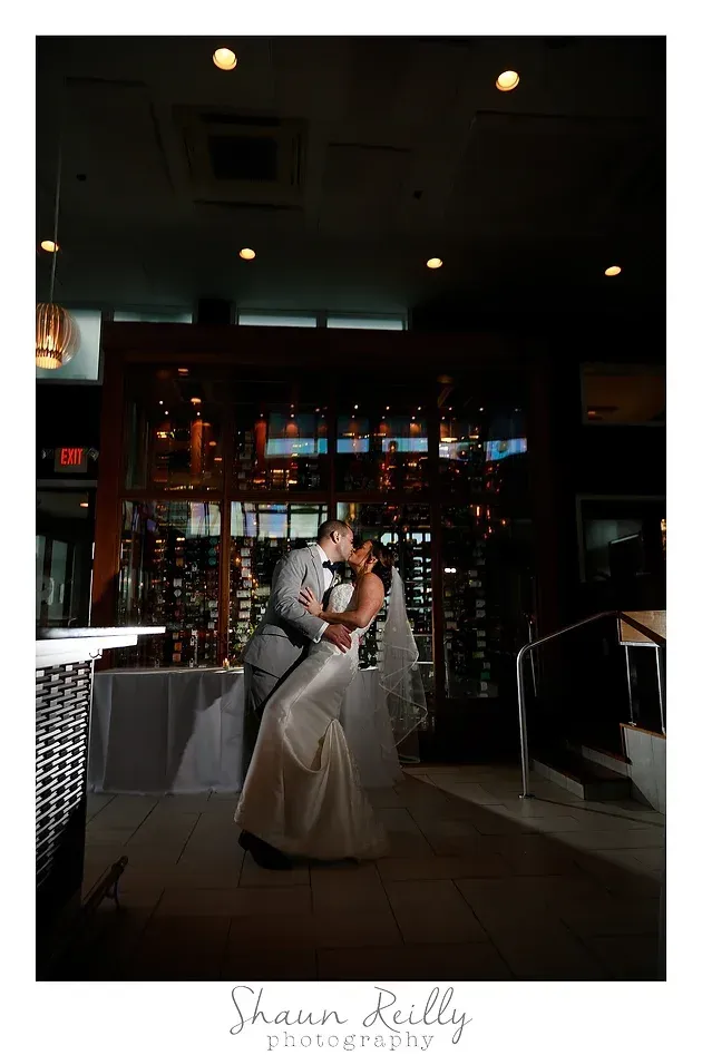 Bride and groom kissing in a dimly lit venue with string lights and decorated tables