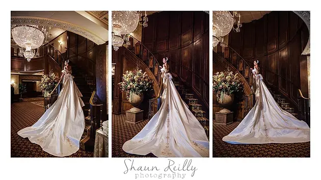 Bride in a white gown with long train posing on a grand staircase in a dark, elegant hall