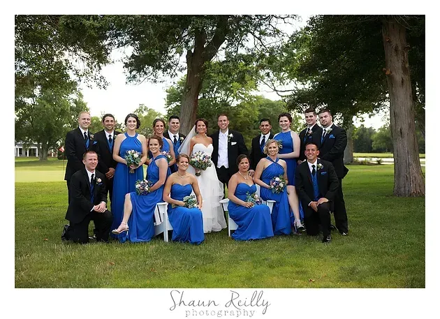 Formal group portrait outdoors in blue and black attire, posed on grass beneath trees