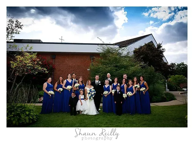 Wedding party in blue dresses and suits posing with bride and groom outdoors in front of a brick building