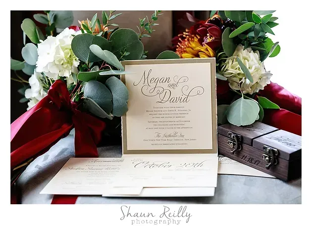Wedding invitation suite with white and burgundy flowers and red ribbon on a table