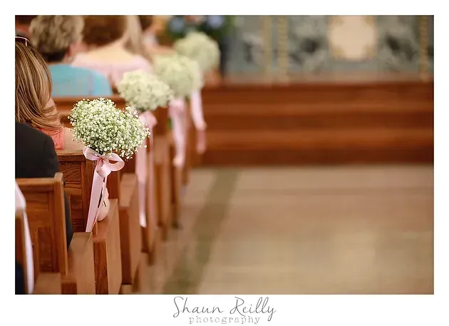 Wedding aisle with wooden pews decorated with white flowers and pink ribbons