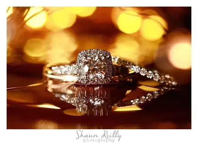 Diamond engagement ring on a reflective surface with warm golden bokeh lights