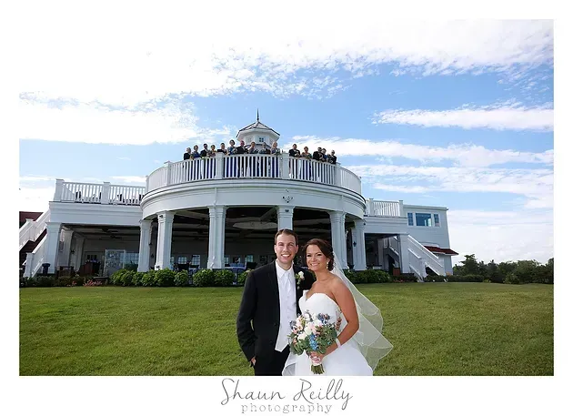 Bride and groom posing on the lawn before a white mansion under a blue sky