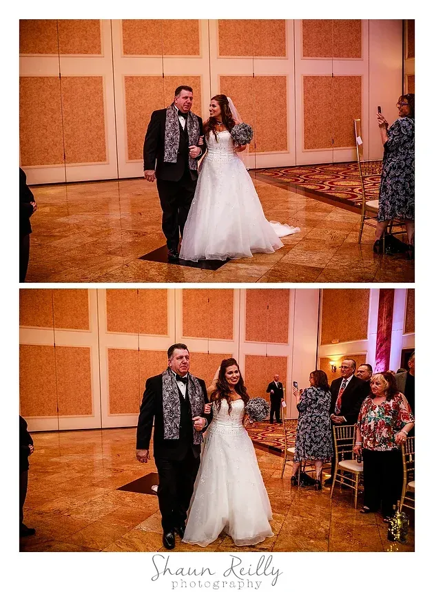 Wedding couple posing in a ballroom during their reception, with seated guests nearby.