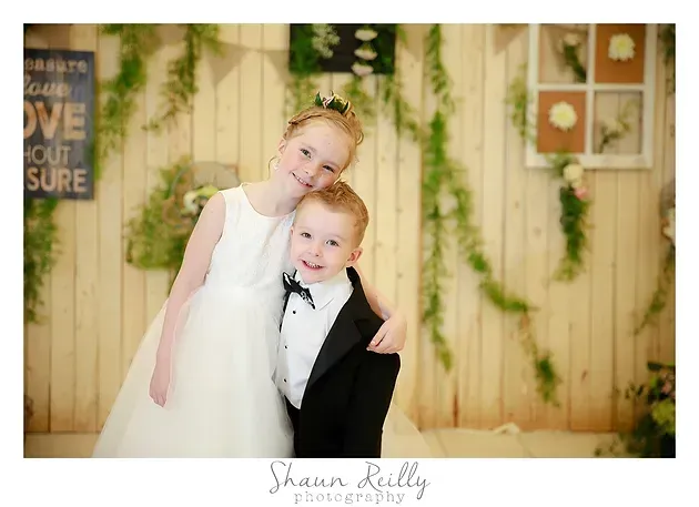 Two children in formal attire posing together in front of a floral backdrop