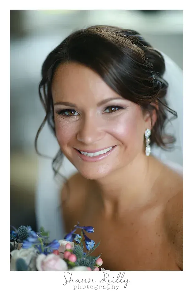 Smiling bride in a white dress with dark hair and pearl earrings, posed in soft natural light
