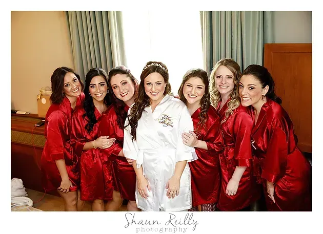 Bridal party in red robes gathered around bride in white robe indoors